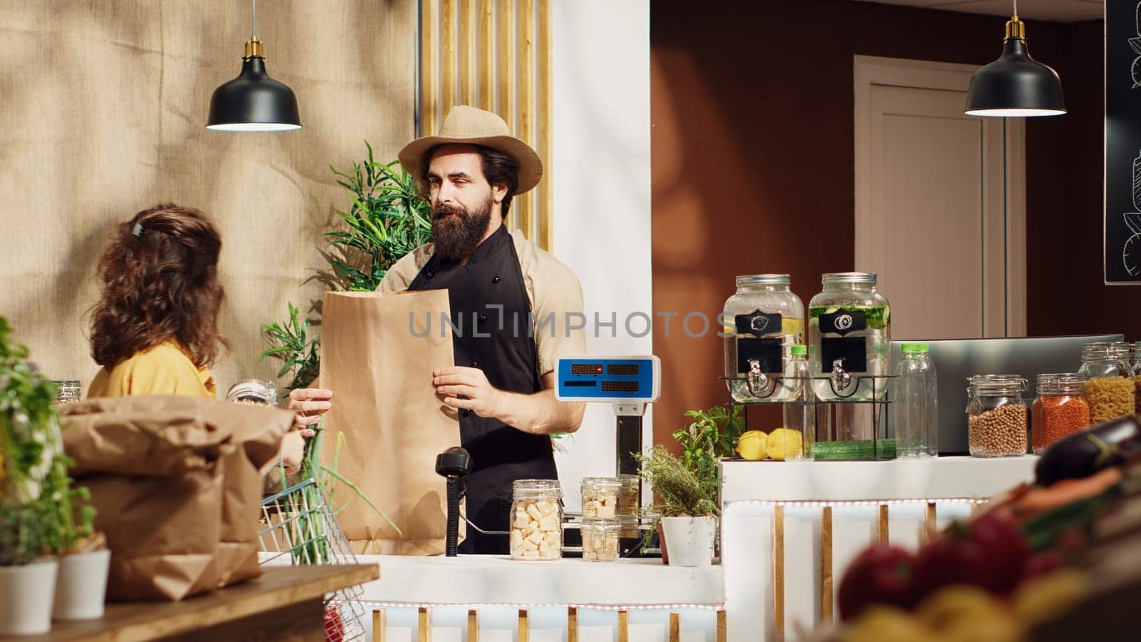 Zero waste supermarket vendor using paper bag to prepare customer groceries, waiting for delivery man to pick up order. Local neighborhood store seller adding pumpkins to shopping bags