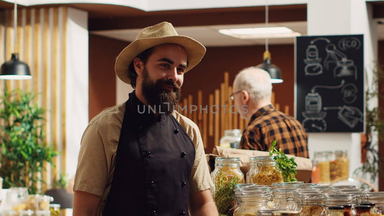 Portrait of happy zero waste supermarket owner using recyclable glass containers for its bulk products to lower climate impact. Cheerful local neighborhood shop entrepreneur arranging merchandise