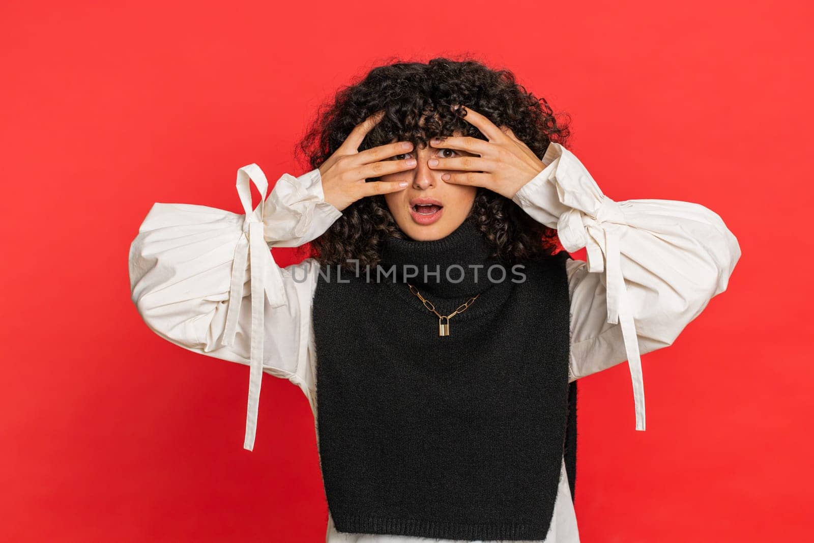 Don't want to look at this, awful. Afraid shocked Caucasian woman with curly hair closing eyes with hand showing stop gesture, confused shy scared reject to watch. Girl isolated on red background