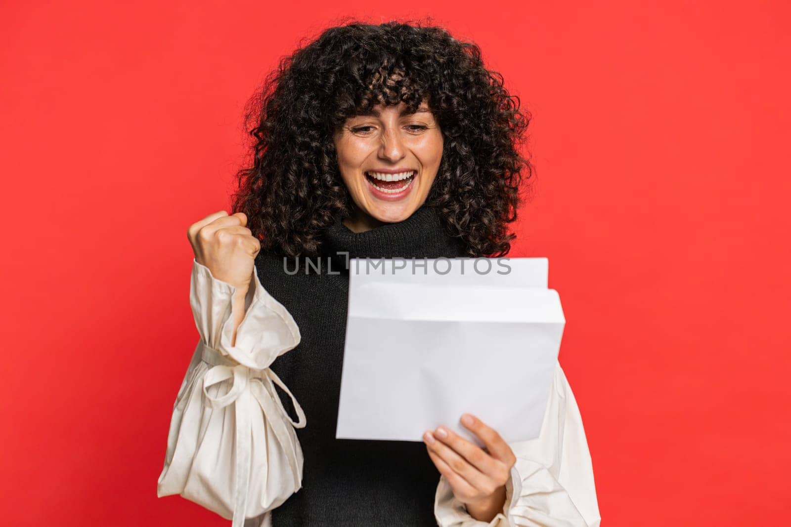 Young woman with curly hair open envelope take out letter reads it feel happy. Career growth advance promotion, bank loan approve, monetary award, long-awaited invitation great news on red background