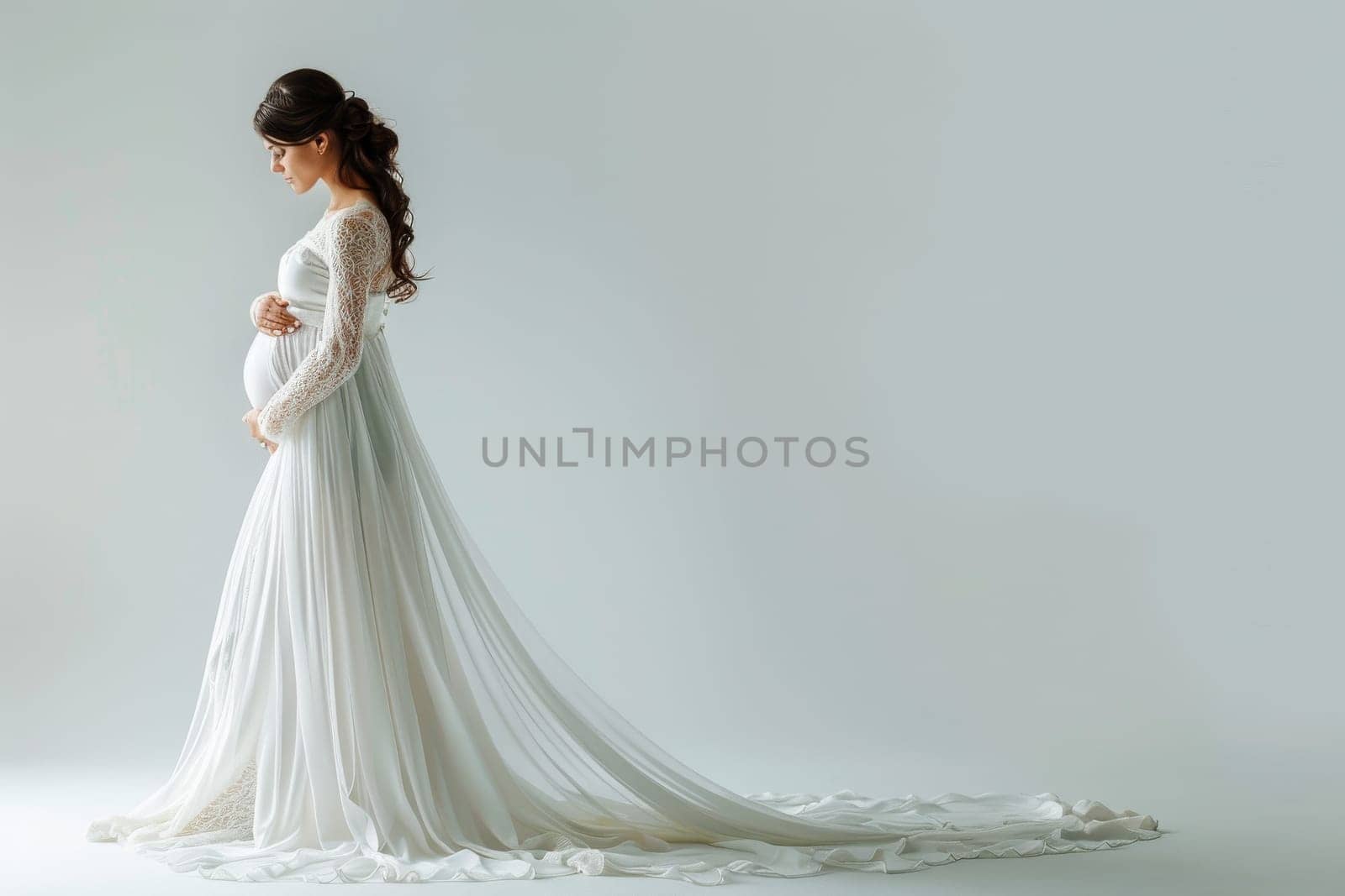 A pregnant woman stands in front of a white background wearing a white gown. The gown is long and flowing, and the woman is in a state of contemplation. Concept of serenity and contemplation