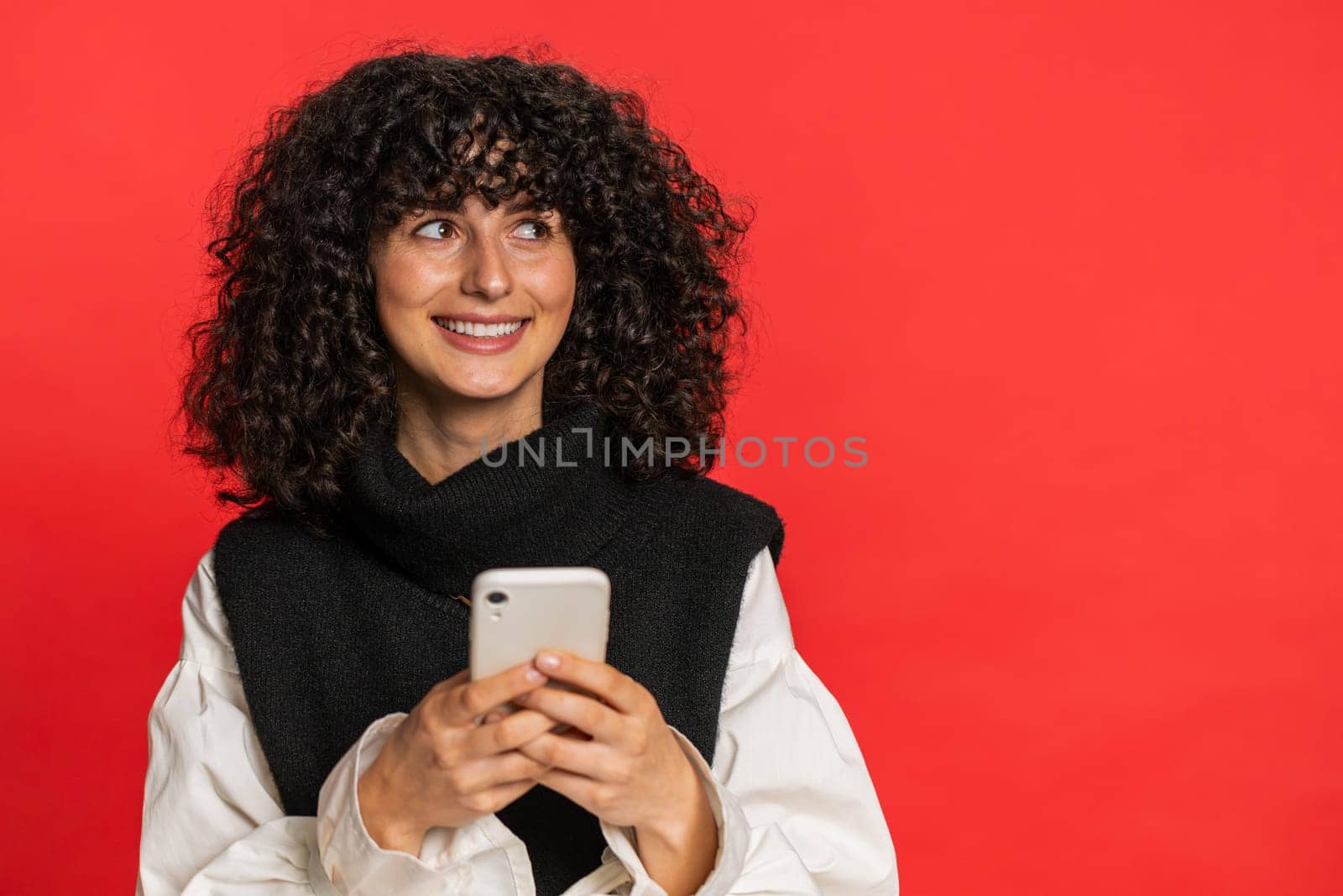 Caucasian woman texting share sms messages content on smartphone social media applications online, watching relax movie browsing. Young girl uses mobile phone smile isolated on red background indoors