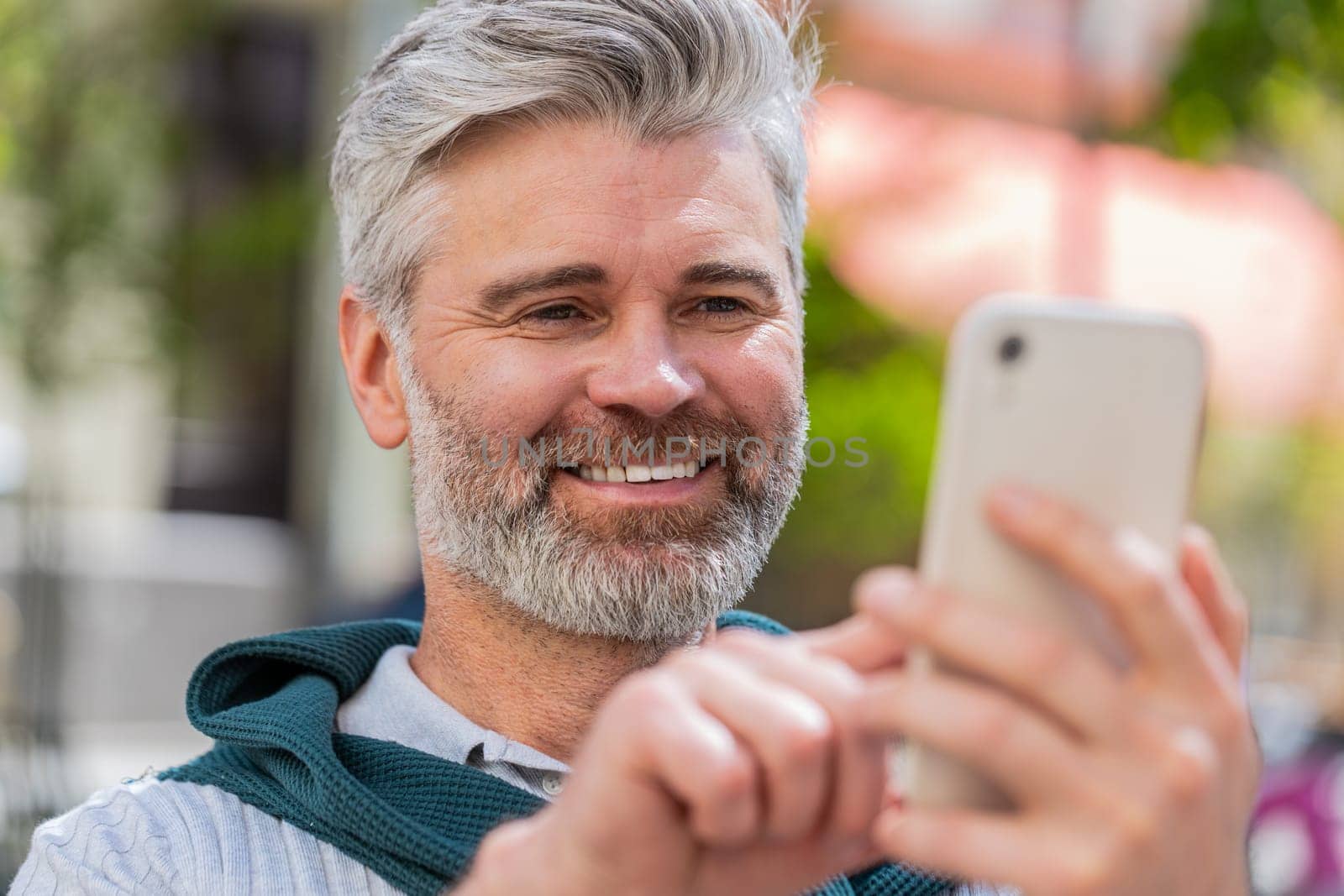 Handsome mature man using smartphone typing text messages tired looking up thinking and browsing internet social media web app working chatting online outdoor. Guy in urban city street. Lifestyles.