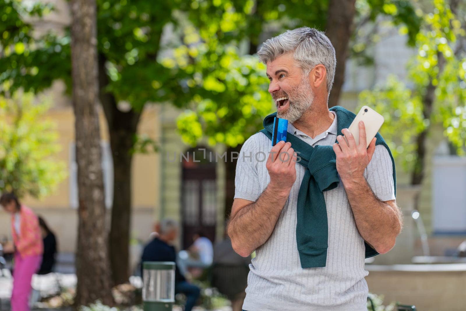 Shocked Caucasian man trying to pay online shopping with smartphone blocked credit card. Annoyed bearded mature tourist on street buying bank refuse problem unsuccessful payment lack of money balance.