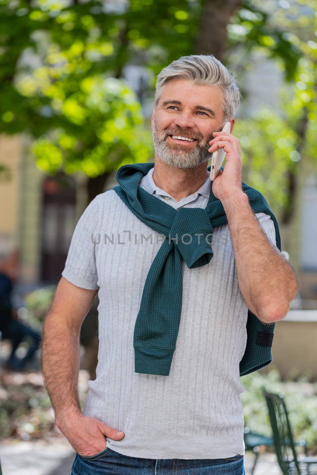 Bearded mature man tourist having remote conversation communicate speaking by smartphone with friend talking on phone unexpected good news gossip on urban city street. Town lifestyles outdoors.