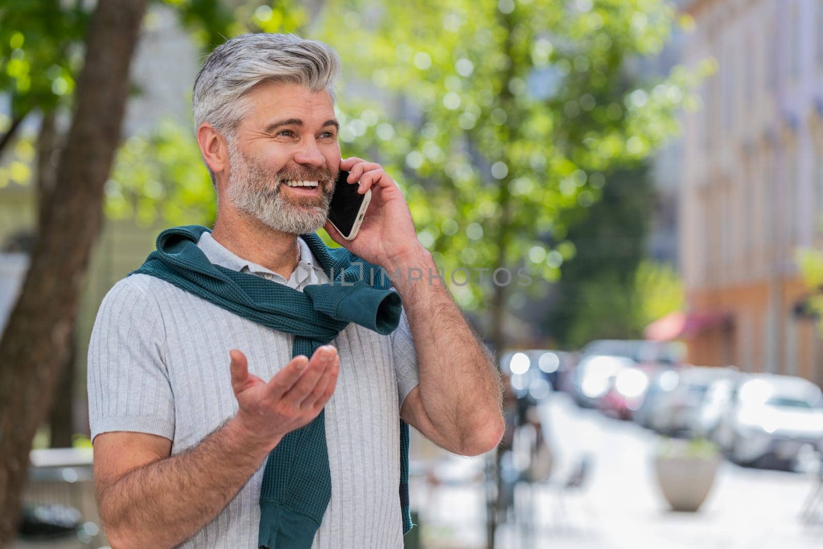 Bearded mature man tourist having remote conversation communicate speaking by smartphone with friend talking on phone unexpected good news gossip on urban city street. Town lifestyles outdoors.