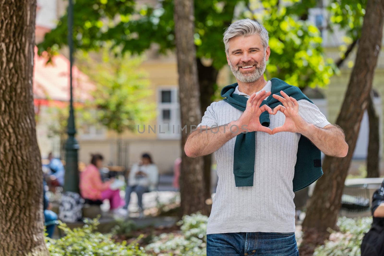 I love you. Caucasian middle-aged man makes symbol of love showing heart sign to camera, express sincere romantic positive feelings. Charity, gratitude, donation. Mature guy on urban city street park.