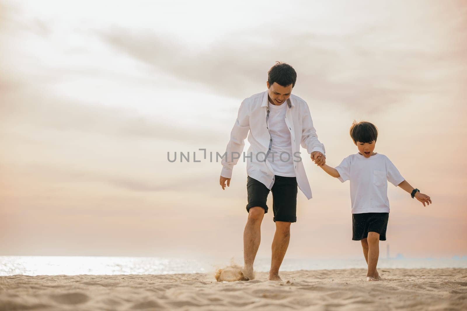 Beach fun with a cheerful Asian father and son running hand in hand. Laughing playing and enjoying the sun this family moment is full of joy and togetherness.