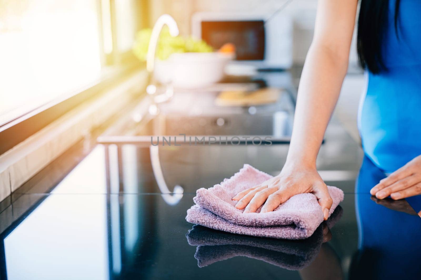 Young housewife smiles while disinfecting her kitchen table with a rag and detergent. Emphasizing routine cleaning and care for a sanitized living space. Wiping cloth kitchen