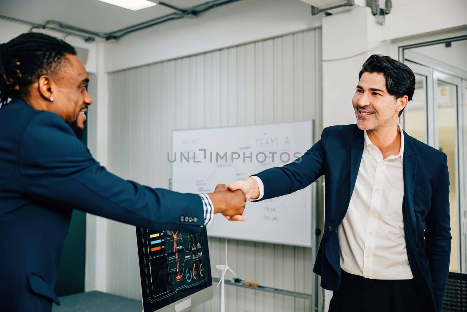 In an office setting, a mature businessman congratulates a younger colleague with a handshake, signifying a successful agreement and partnership. Businessmen shake hands during a leadership meeting.