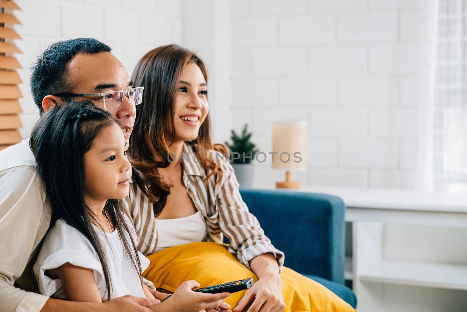 Asian family with kids finds relaxation and togetherness watching TV on sofa in their grooved modern living room. father mother son and daughter create precious family moments filled with smiles