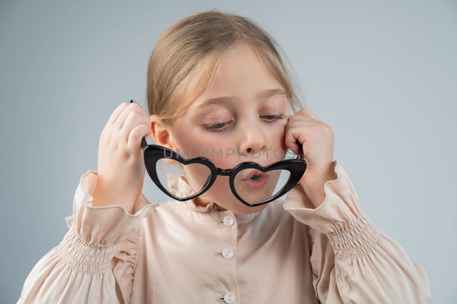 Portrait of a cute little girl blowing on heart-shaped glasses on a white background