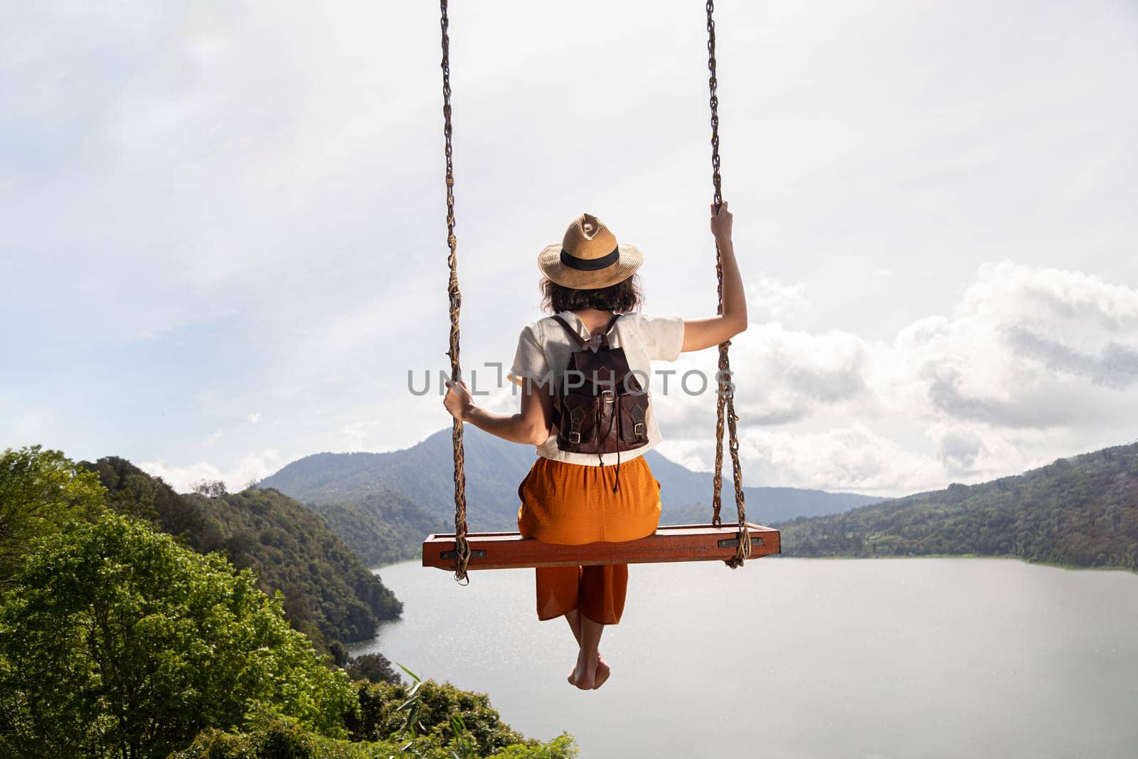 Young female tourist enjoying landscape sitting on a swing in Bali, Indonesia. Vacation concept.