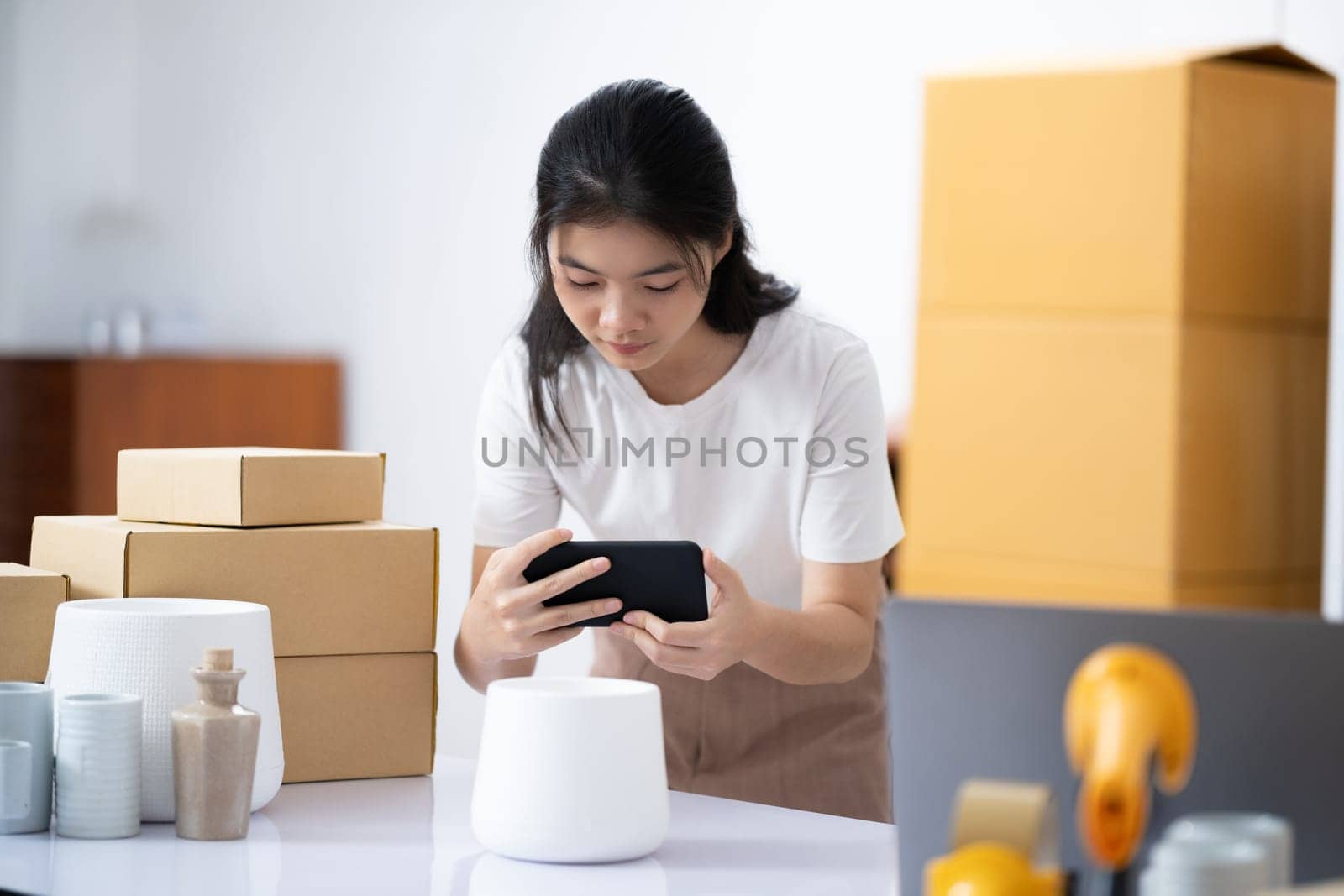 Young women taking photo of product with cell telephone or smartphone digital camera for post to sell online on the Internet and preparing pack product box. Selling online ideas concept
