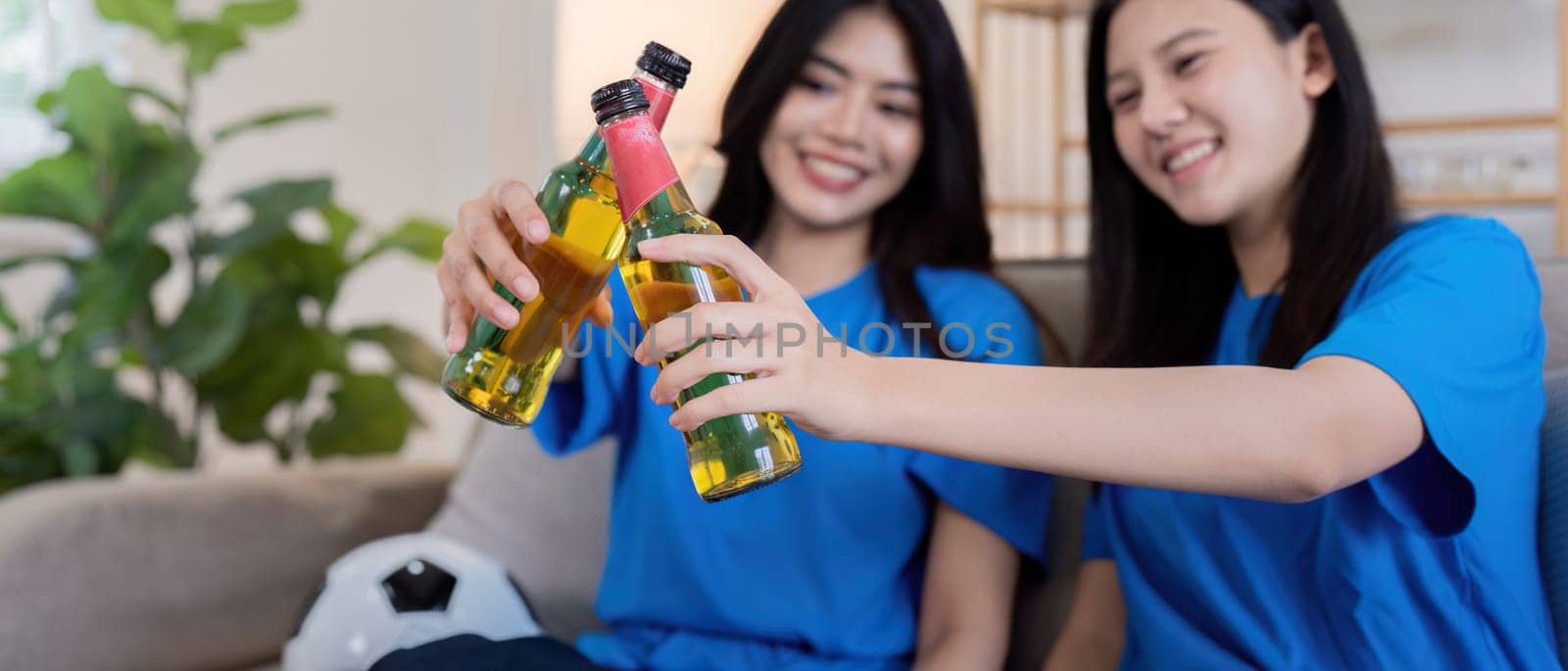 Lesbian couple cheering and toasting for Euro football at home with drinks. Concept of LGBTQ pride, sports enthusiasm, and celebration.