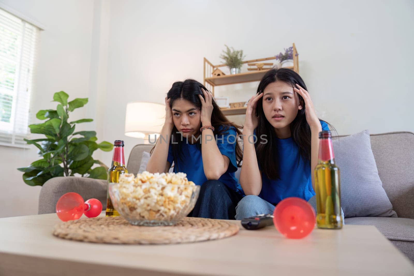 Lesbian couple anxiously watching Euro football match at home with popcorn and drinks. Concept of LGBTQ pride, sports enthusiasm, and domestic bonding.