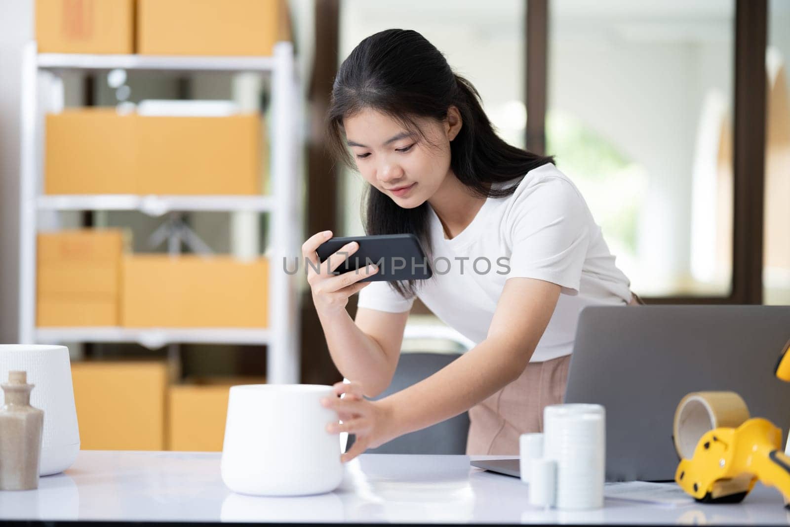 Young women taking photo of product with cell telephone or smartphone digital camera for post to sell online on the Internet and preparing pack product box. Selling online ideas concept