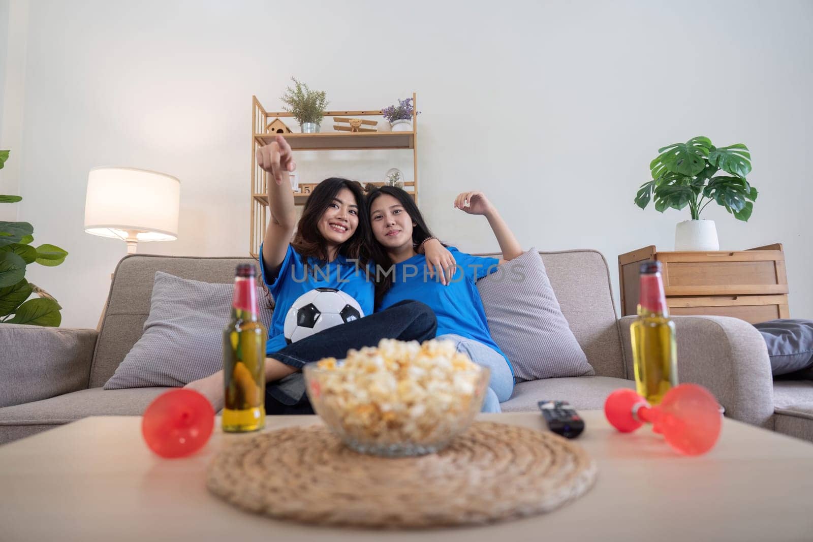 Lesbian couple cheering for Euro football at home with drinks and popcorn. Concept of LGBTQ pride, sports enthusiasm, and celebration by nateemee