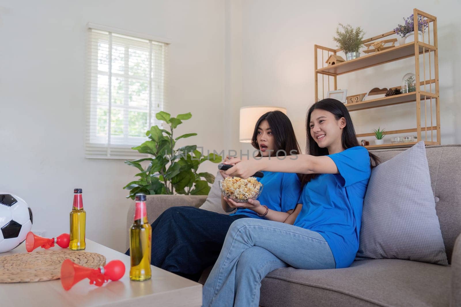 Lesbian couple cheering for Euro football at home with snacks and beer. Concept of LGBTQ pride, sports enthusiasm, and domestic leisure.