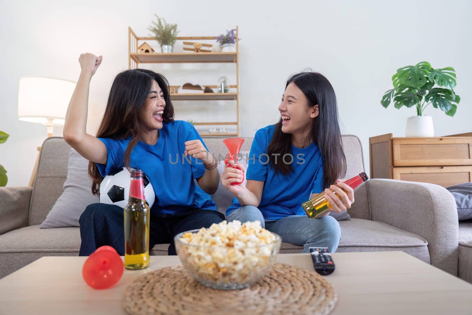 Lesbian couple cheering while watching Euro football match at home with drinks and popcorn. Concept of LGBTQ pride, sports enthusiasm, and celebration.