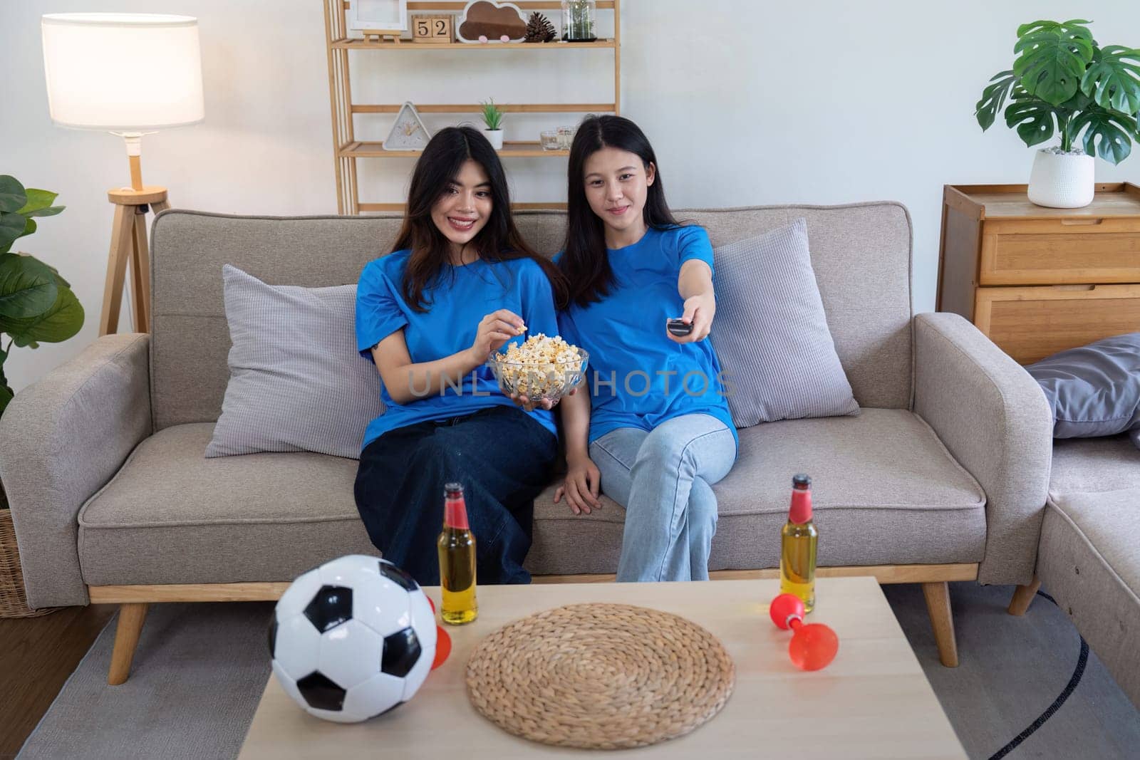 Lesbian couple cheering for Euro football at home with snacks and drinks. Concept of LGBTQ pride, sports enthusiasm, and domestic leisure.