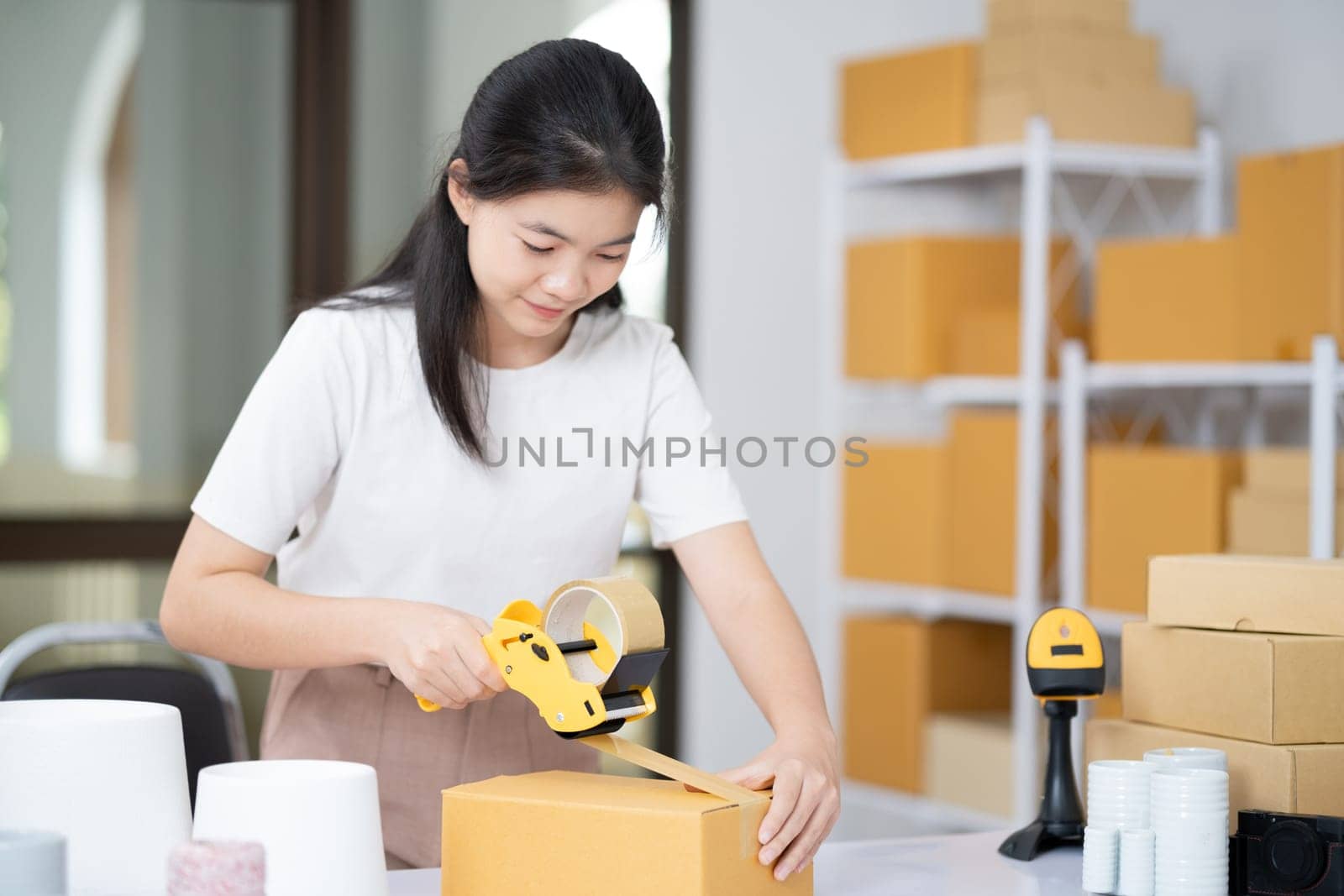 Young Asian business entrepreneur sealing a box with tape. Preparing for shipping, Packing, online selling, e-commerce concept.