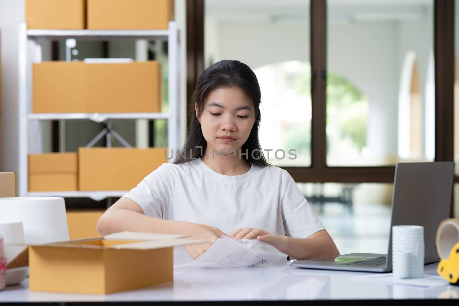 Young woman packing product for customer with cardboard box.
