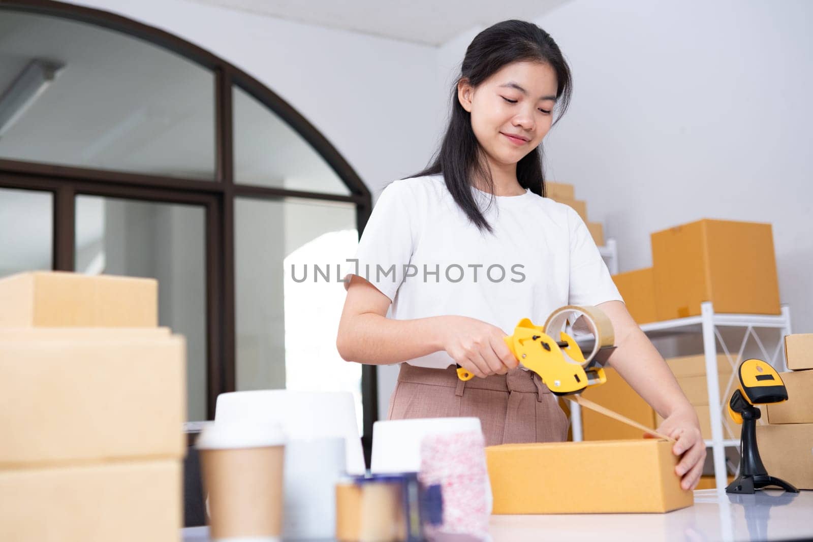 Young Asian business entrepreneur sealing a box with tape. Preparing for shipping, Packing, online selling, e-commerce concept.