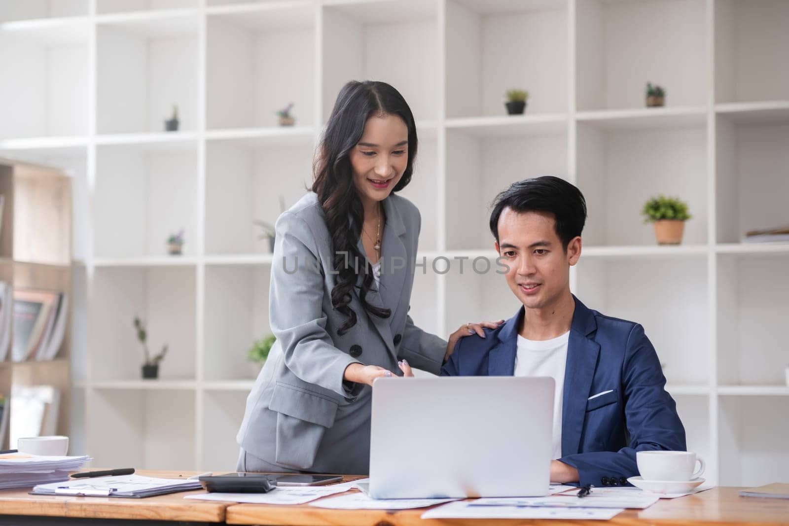 A young businessman and a female Asian accountant are discussing financial accounting and business planning together in the office. by wichayada