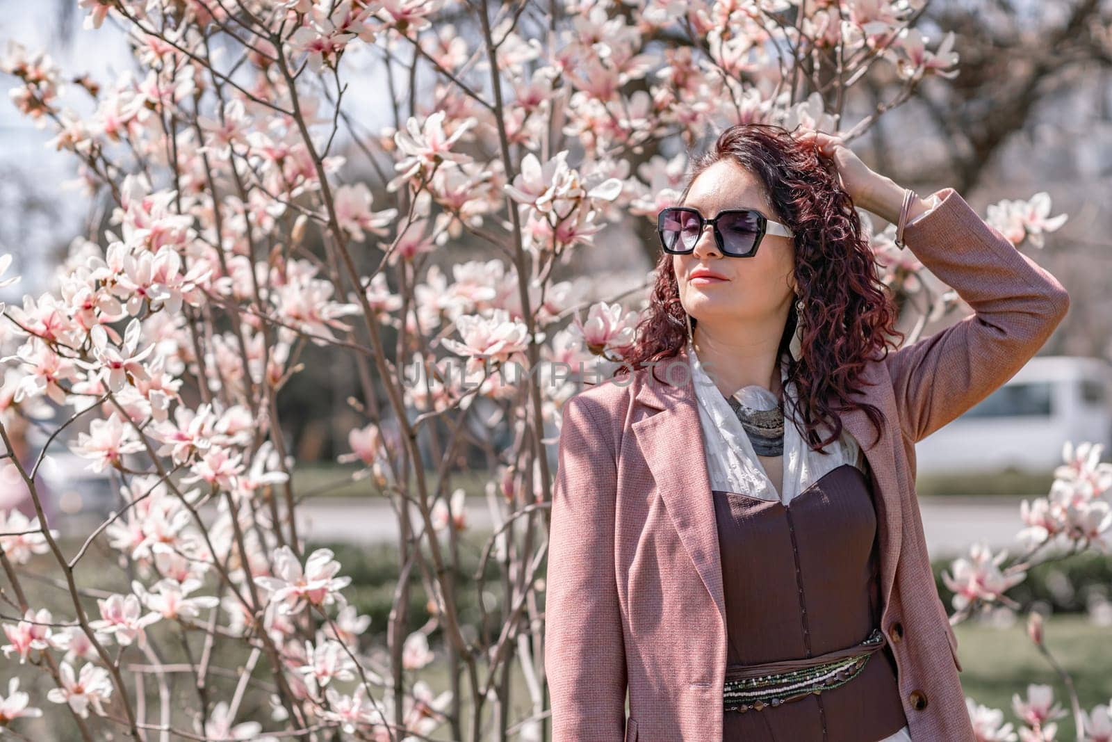 Magnolia park woman. Stylish woman in a hat stands near the magnolia bush in the park. Dressed in white corset pants and posing for the camera. by Matiunina