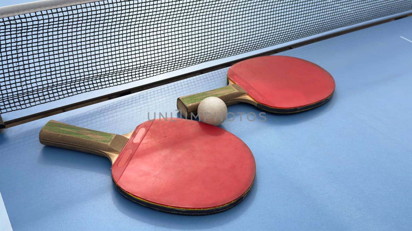 Two table tennis rackets and balls on a blue table with net. High quality photo