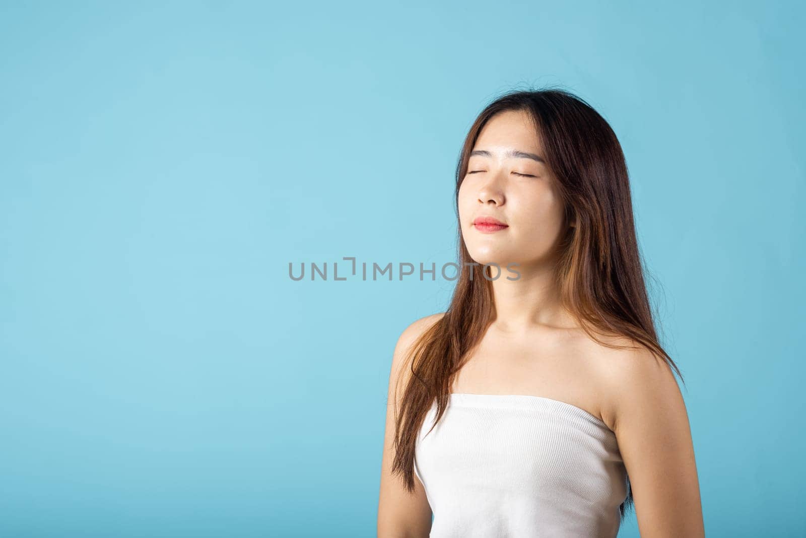 Front portrait of Asian young woman beautiful face closed eyes and smiling studio shot isolated on blue background, close up face of happy female healthy sleeping, beauty care calm and relaxed