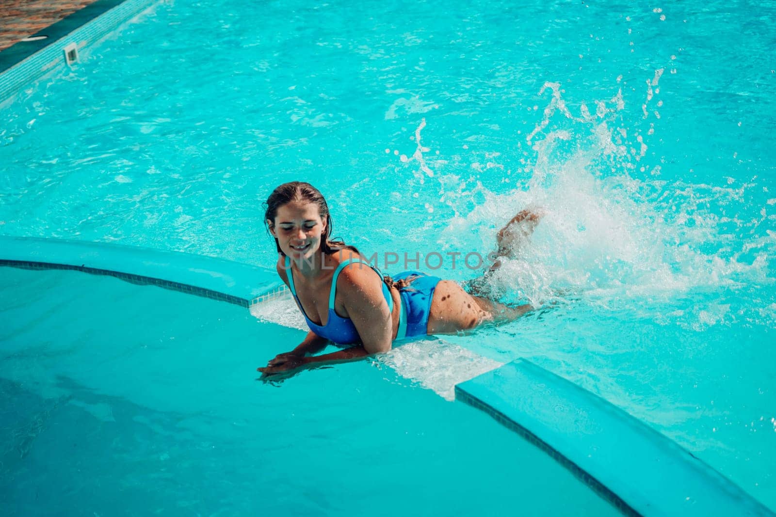 A woman is in the water, smiling and enjoying herself. The water is blue and the pool is surrounded by a white ledge