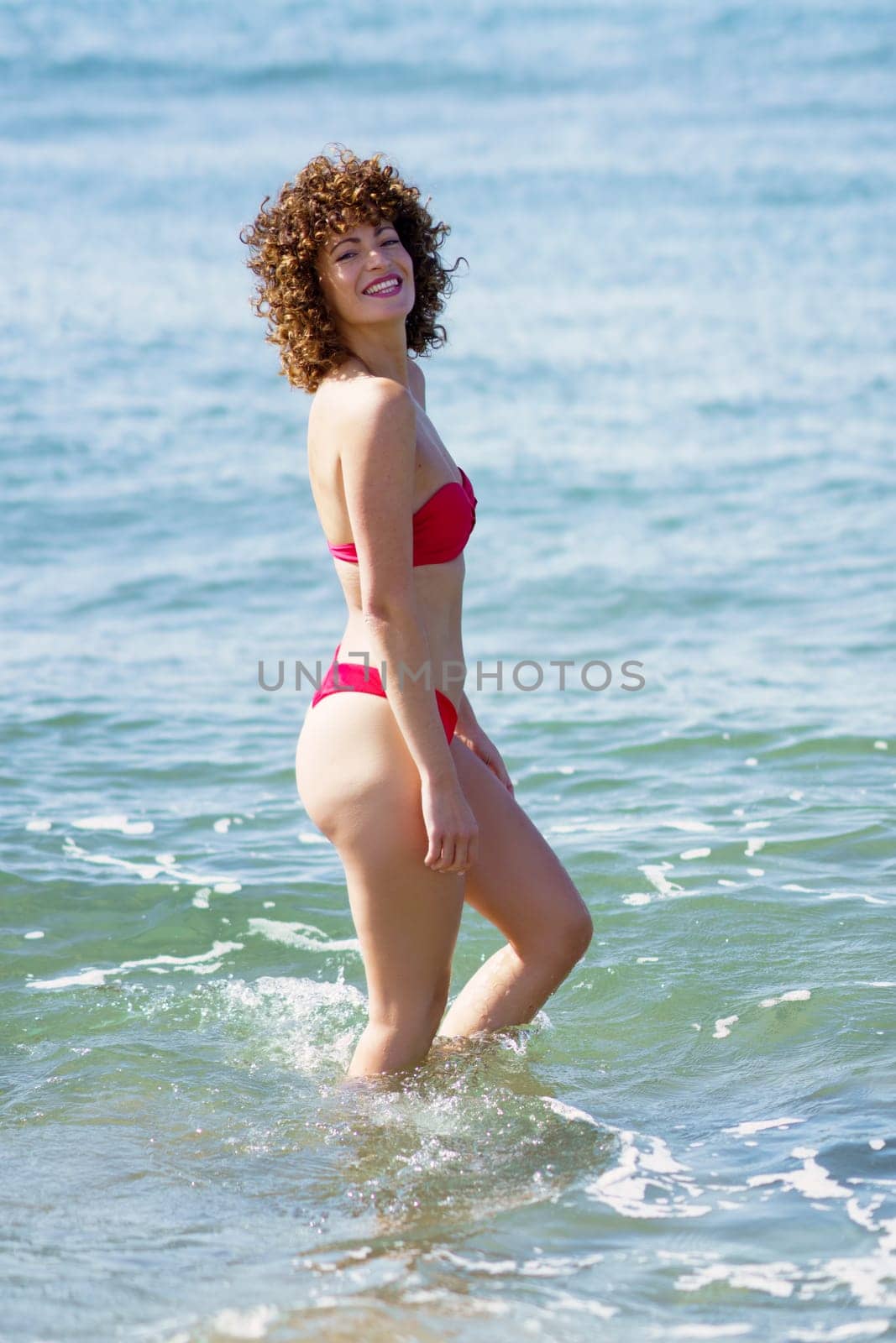 Cheerful woman in swimwear smiling while walking in sea by javiindy