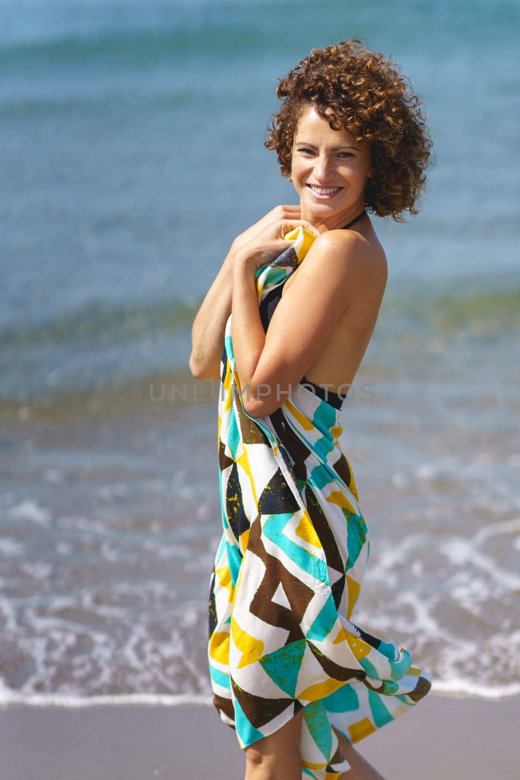 Smiling woman in stylish dress standing on sandy beach by javiindy