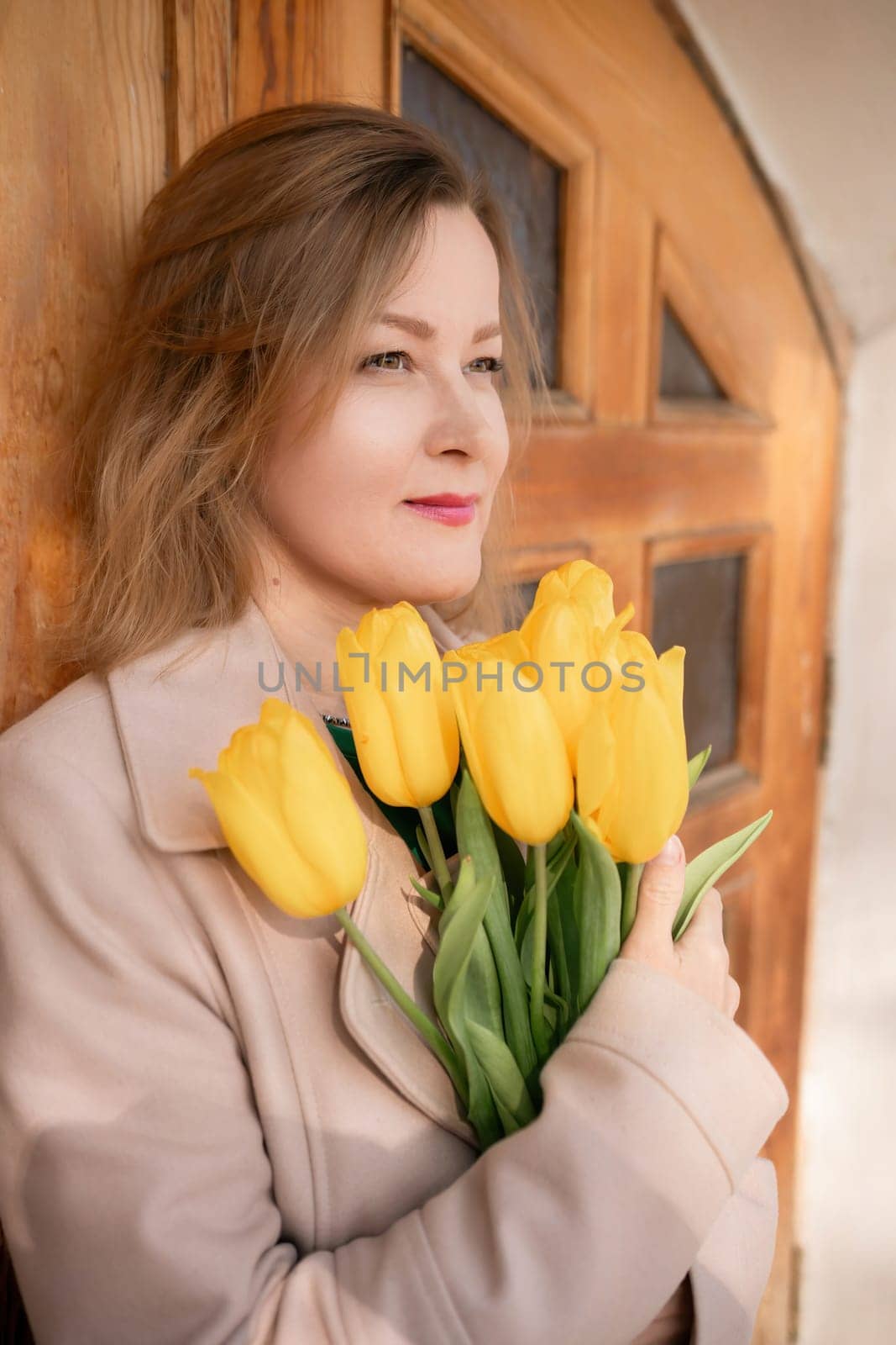 A woman is holding a bouquet of yellow tulips. She is wearing a tan coat and a green shirt. by Matiunina