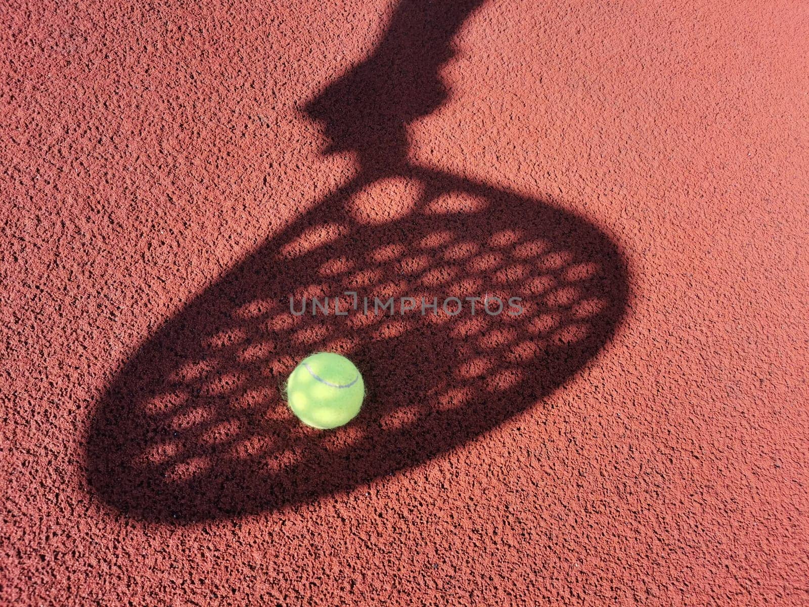 High angle of yellow ball placed on court and covered with shadow of crop person holding padel racket. High quality photo