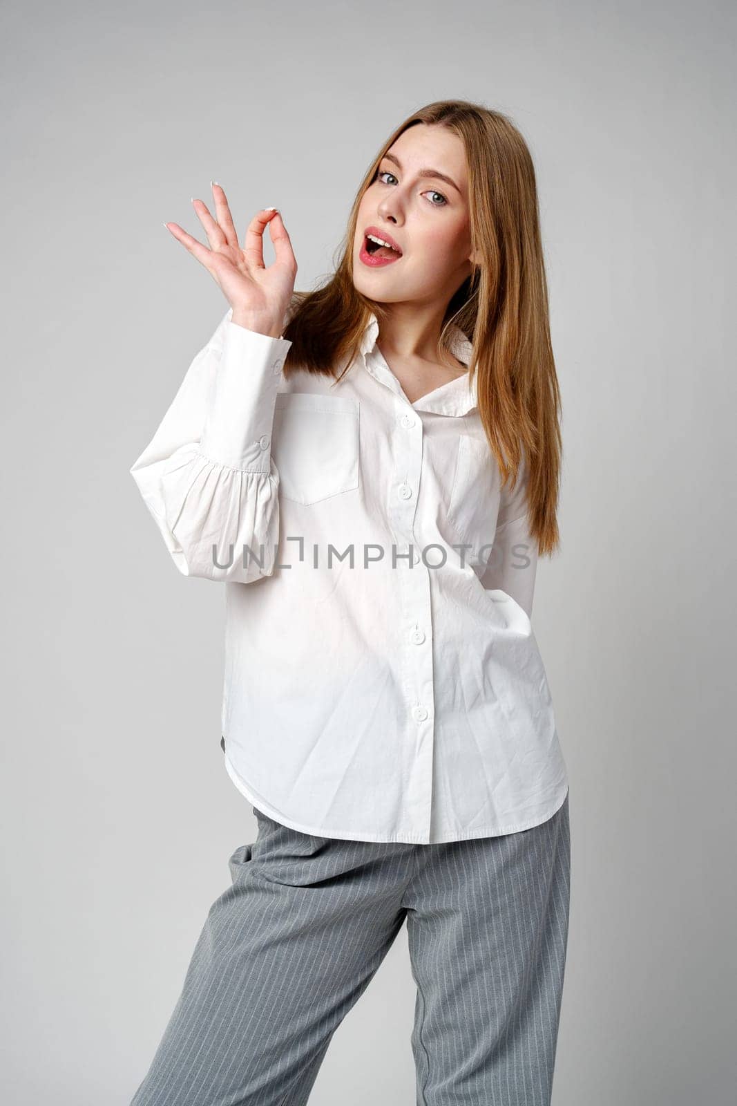 Young Woman Gesturing OK Sign With Hand Against a Neutral Background in studio