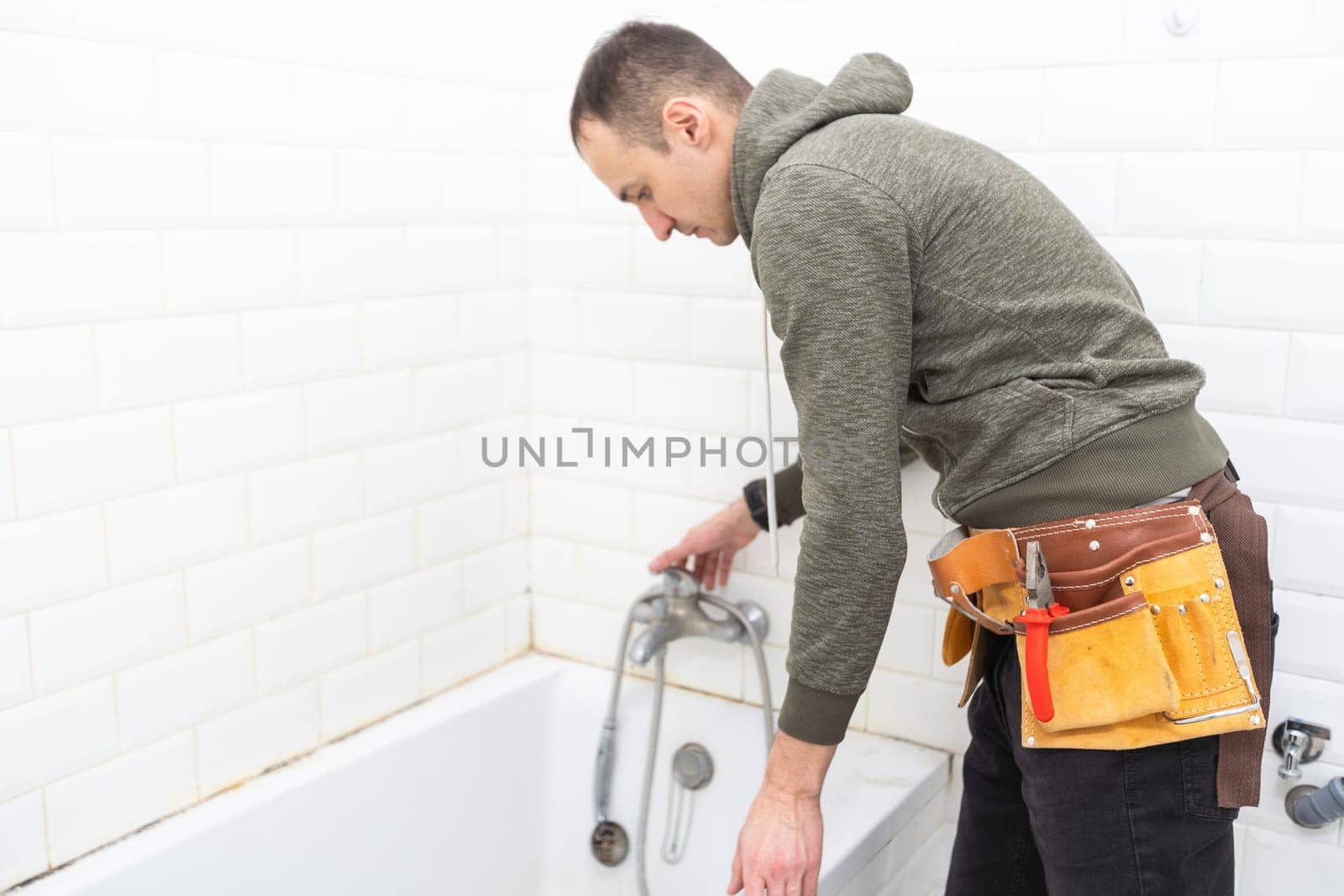 A male plumber with wrench repairs the faucet in the bathroom. replacement and maintenance of plumbing. handyman service. small business. High quality photo