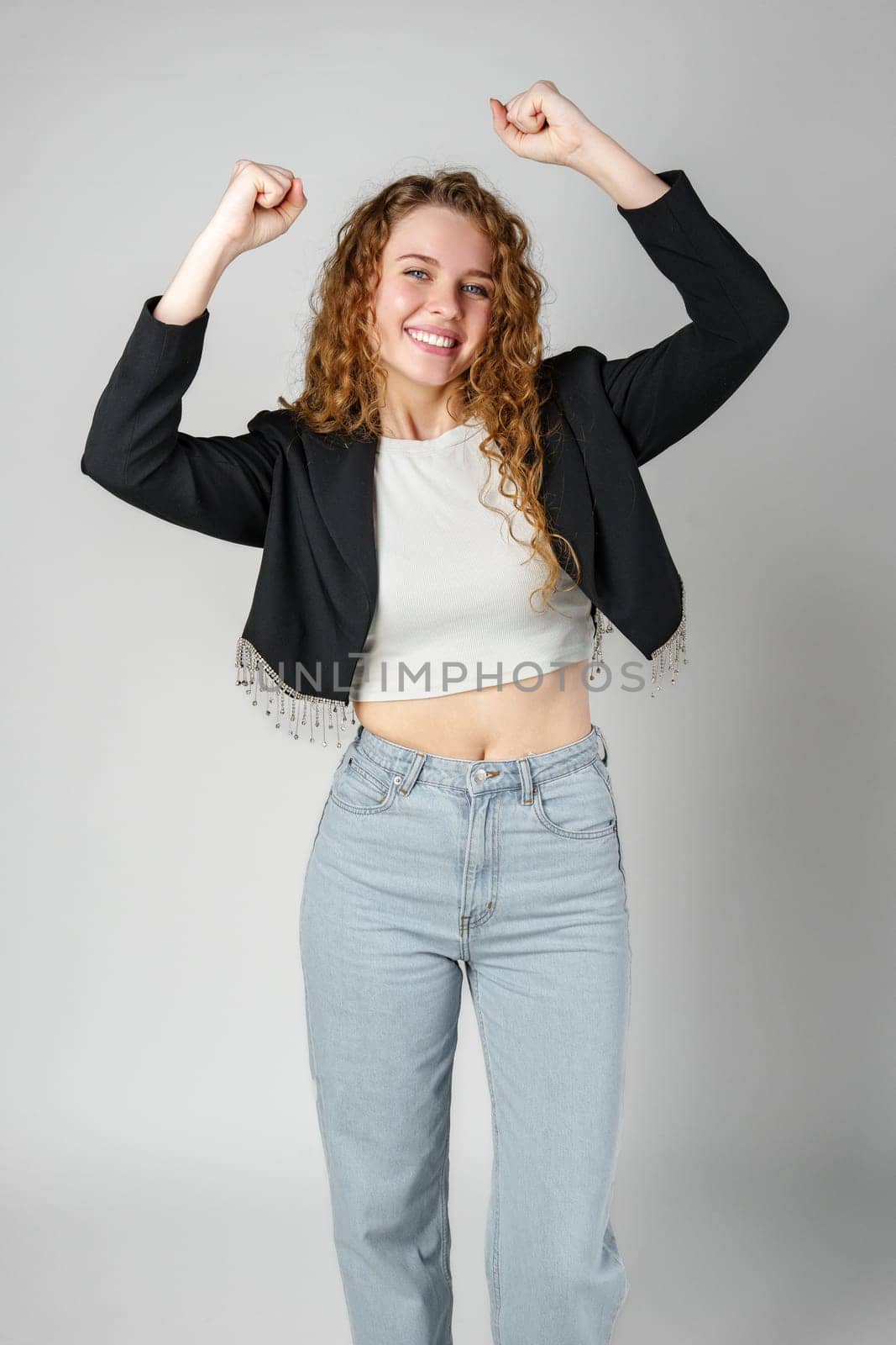 Joyful Young Woman Dancing Alone in Light-Colored Casual Attire Against a Grey Background close up