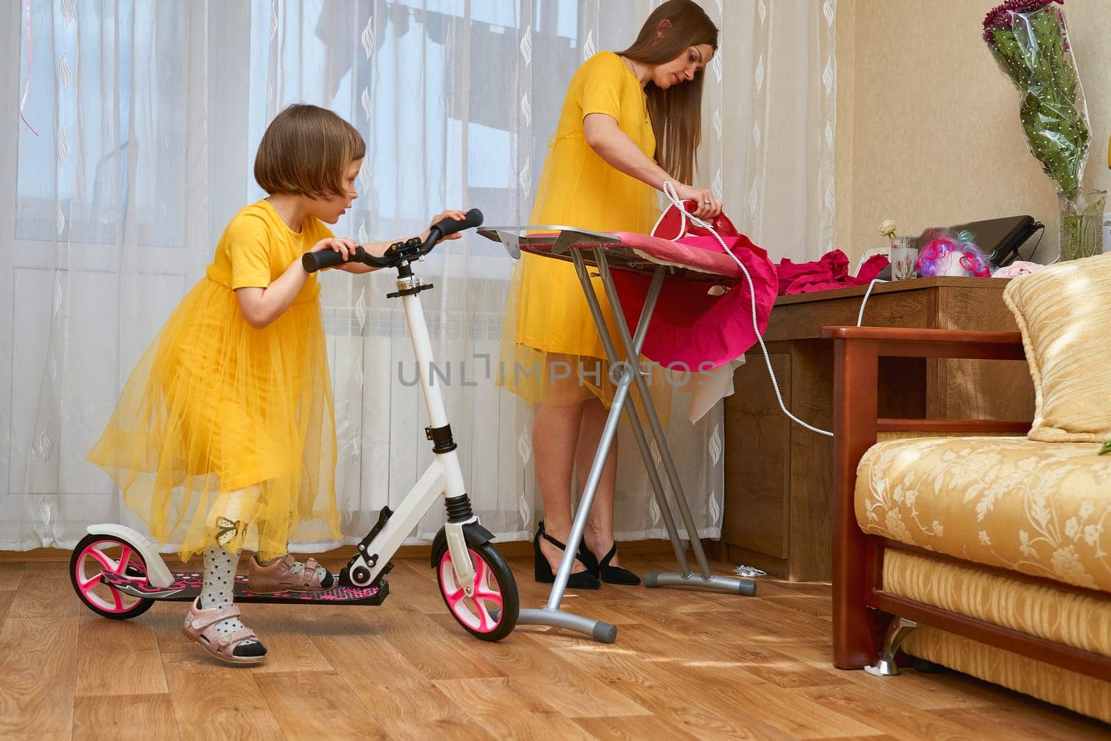 Mom and daughter on a scooter in yellow dresses. Mom irons clothes by jovani68