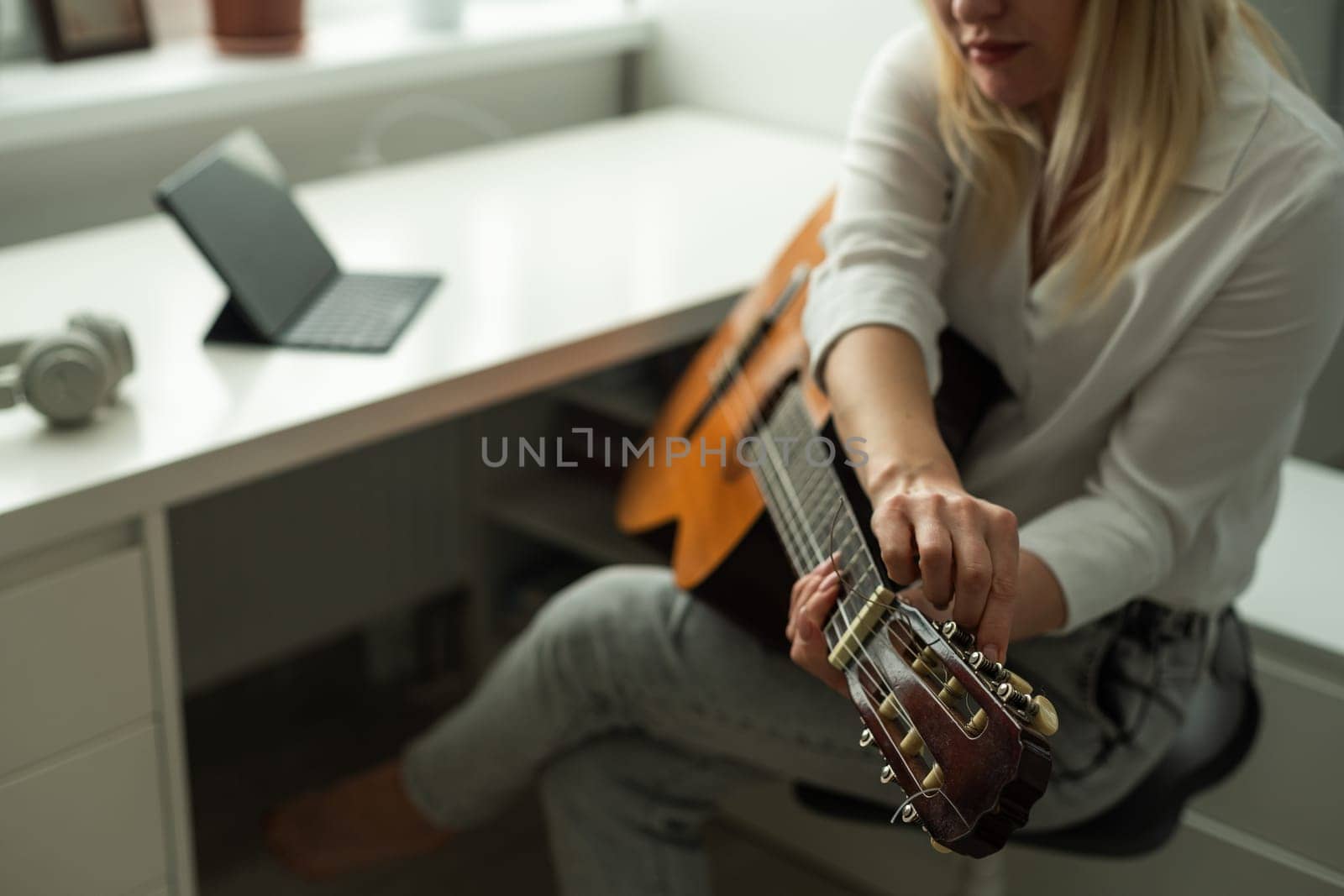 Serene young woman in wireless headphones using acoustic musical instrument while sitting with laptop. High quality photo