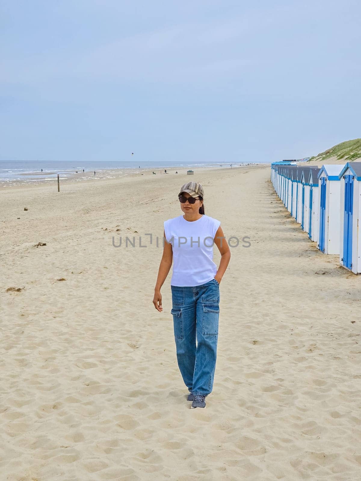 A serene woman walks gracefully along the Texel beach, her steps leaving imprints in the sand. She wears jeans and a white tee shirt, enjoying the peaceful ambiance of the coastline by fokkebok