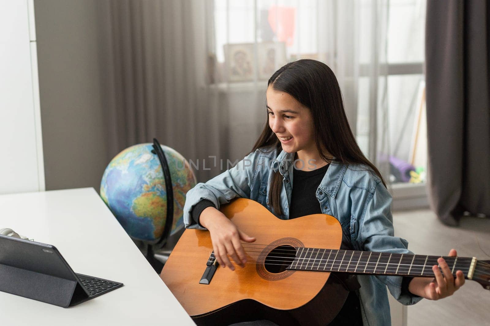 Teenager girl learning to play guitar at home using online lessons. Hobby remote musical education acoustic guitar. Copy space. High quality photo