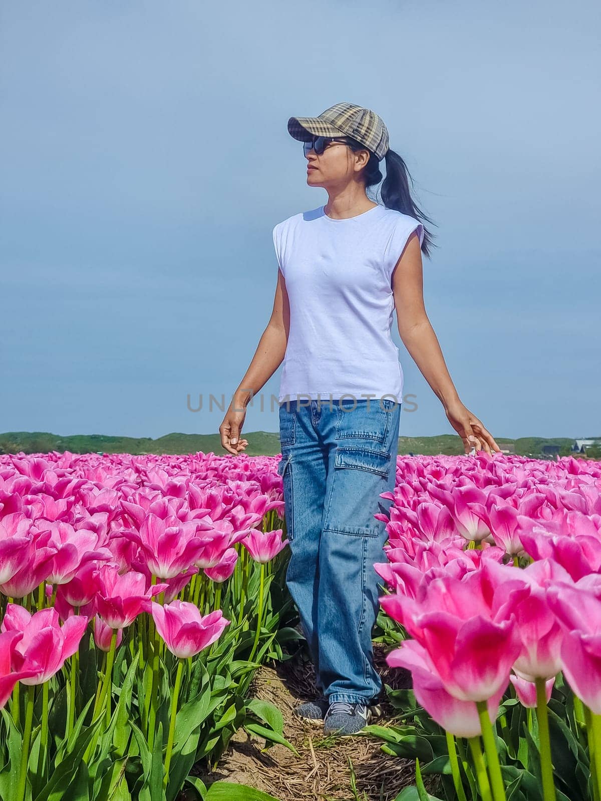 A graceful woman stands elegantly in a vast field filled with vibrant pink tulips, surrounded by a sea of delicate petals by fokkebok