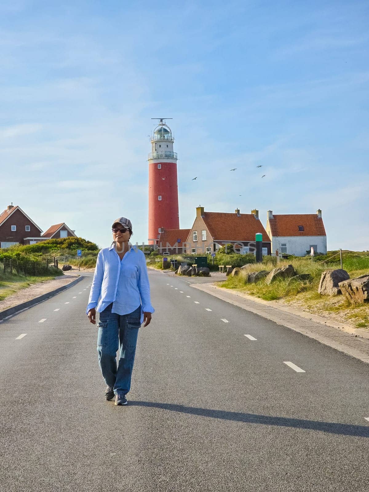 A solitary man walks down a deserted road, with a majestic lighthouse towering in the background, casting a guiding light.