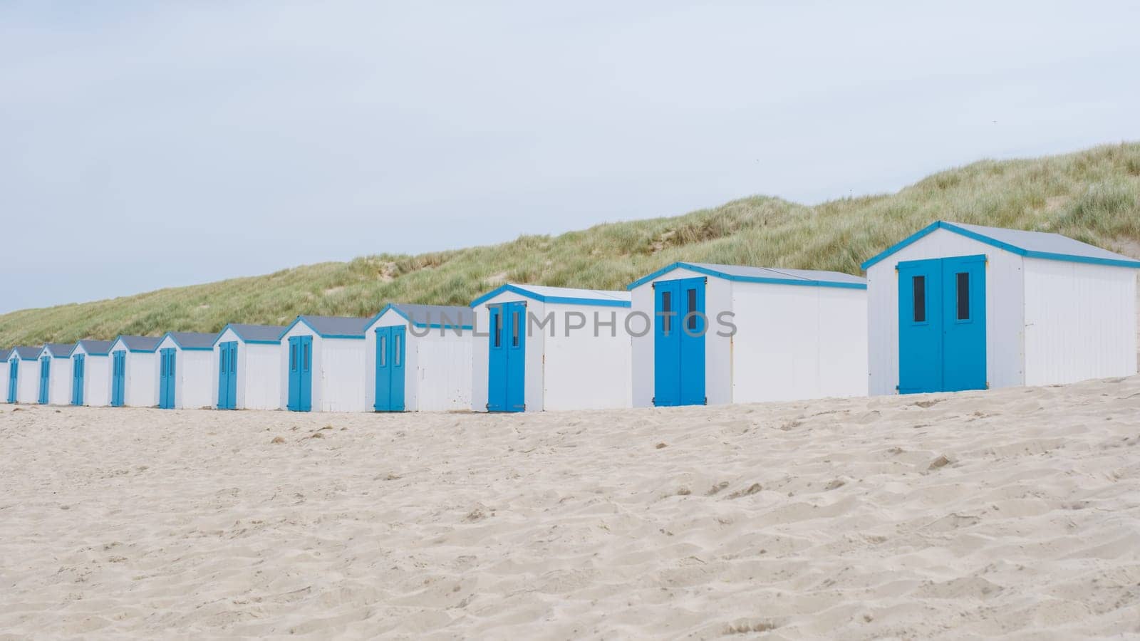 A charming row of beach huts with vibrant blue doors standing on the sandy shores of Texel, creating a picturesque scene against the backdrop of the sea.