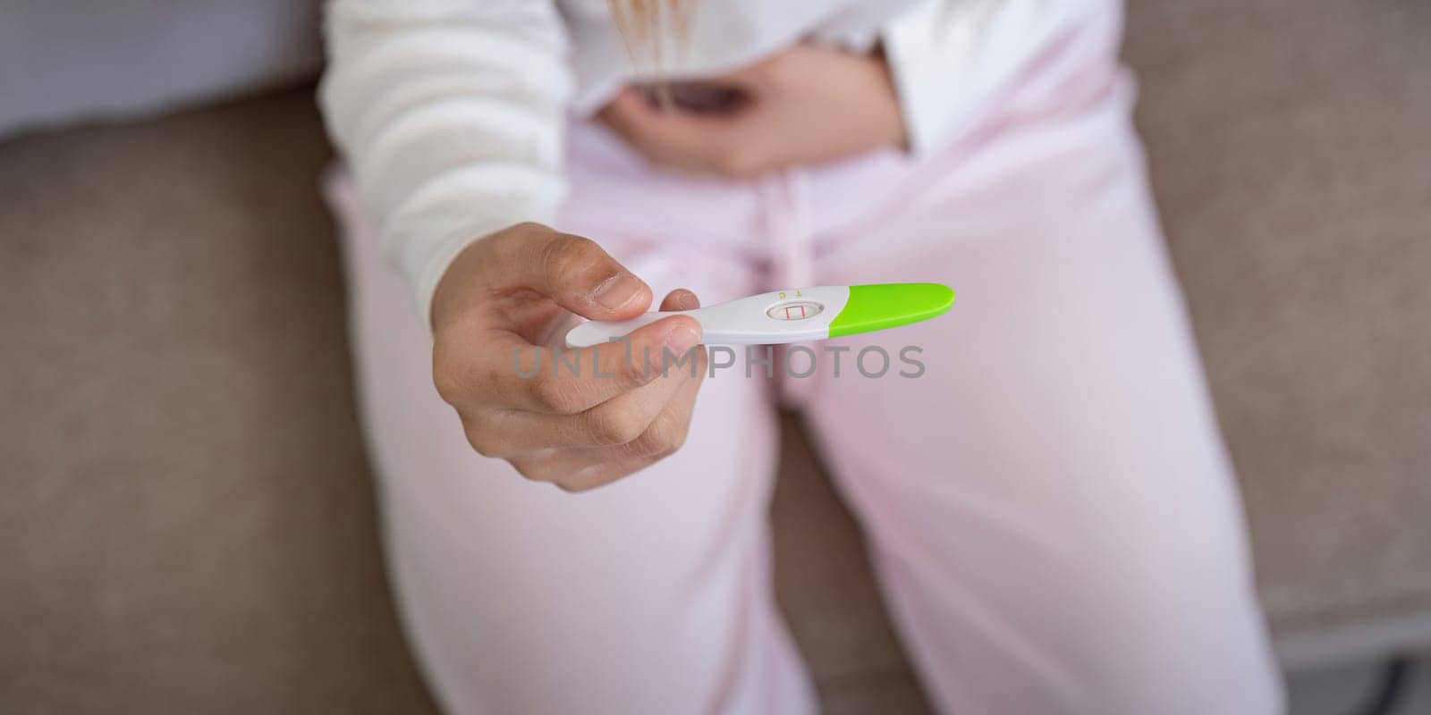Positive pregnancy test held by woman at home, showing happiness. Concept of new beginnings and joyful discovery.