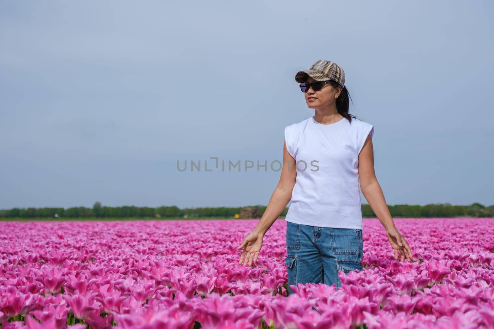 A graceful woman standing amidst a vibrant field of pink tulips in Texel, Netherlands, as the colorful flowers sway with the gentle breeze.