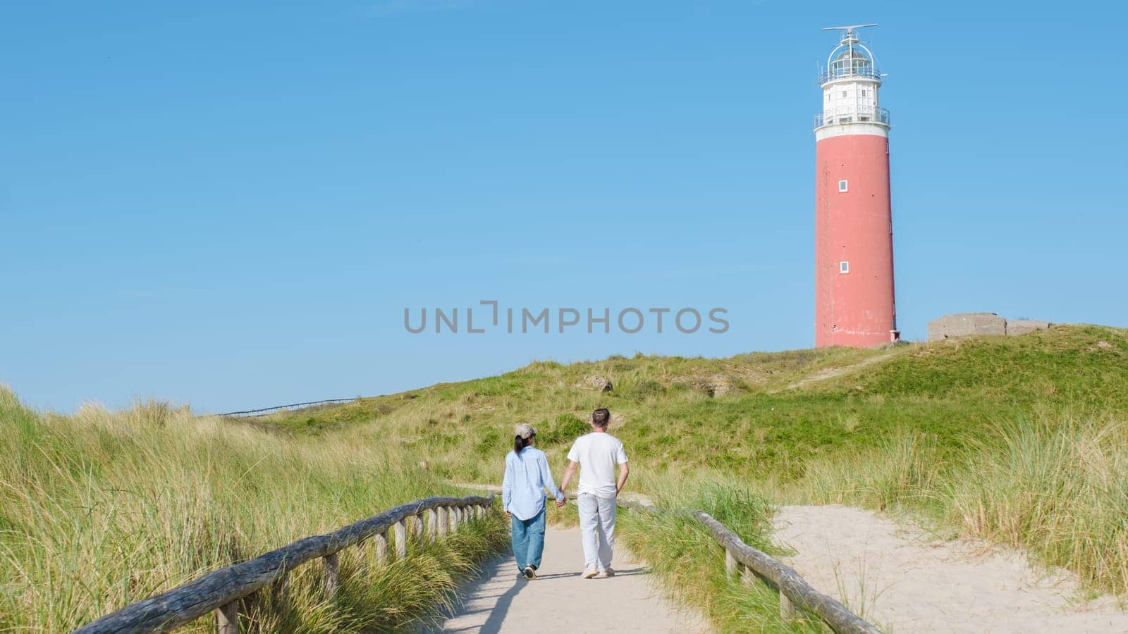A couple leisurely walks along a scenic path near a historic lighthouse in Texel, Netherlands.